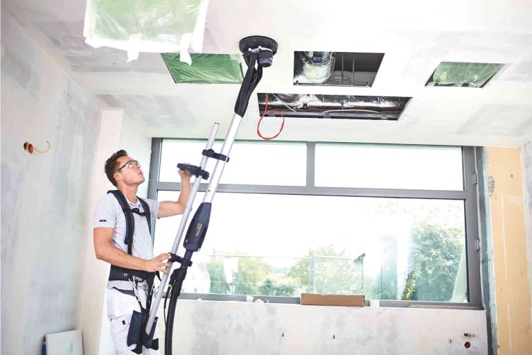 un bricoleur utilisant une ponceuse girafe avec un harnais pour poncer le plafond