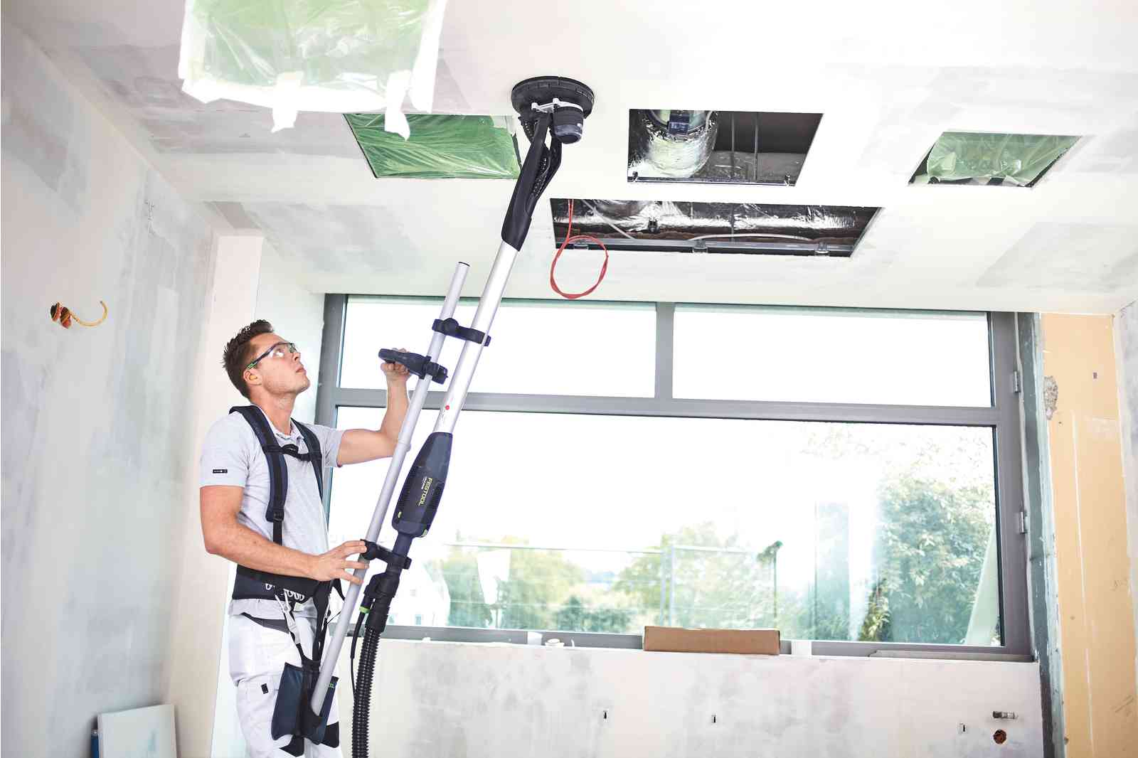 un bricoleur utilisant une ponceuse girafe avec un harnais pour poncer le plafond
