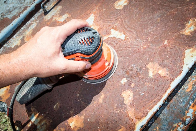 un bricoleur utilisant une ponceuse orange pour enlever la rouille